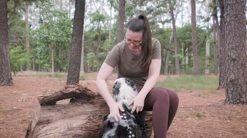 Woman Pets Dog on Log in Forest