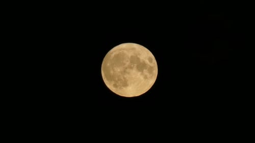 Full orange harvest moon crater surface closeup passing across dark sky