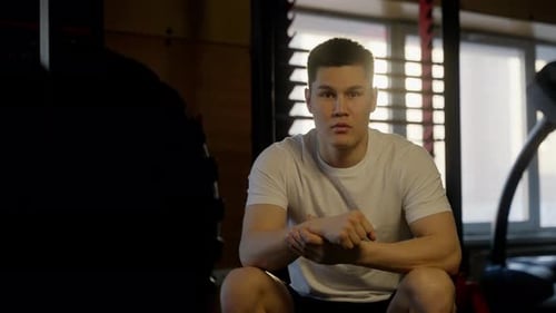 Young Adult Sitting in Gym Examining Wrist