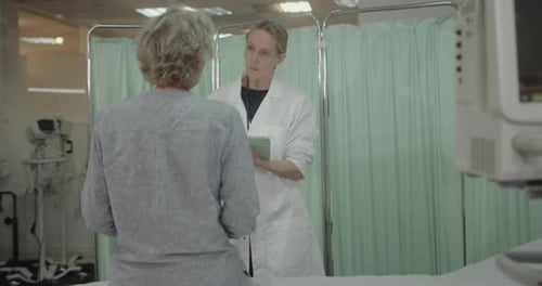 Female Doctor Examining Senior Patient in Hospital, taking notes on Digital Tablet