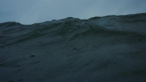 Frontal view of ocean water surface as rain drops fall and wave crashes exploding with power and whi