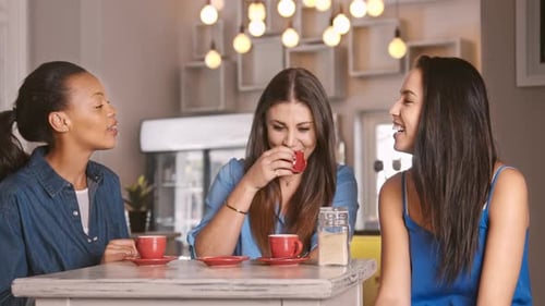 Three friends enjoy coffee laughing at cafe