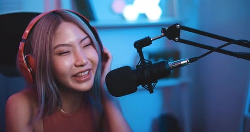 Young Asian woman influencer wearing headphones talking into a microphone while recording a radio