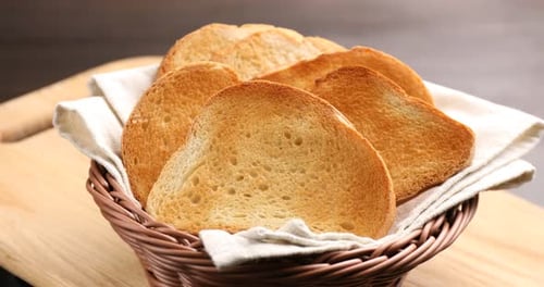 Rebanadas de pan tostado dorado en una cesta de mimbre sobre la mesa, primer plano
