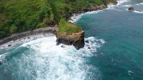 Waves crashing on rocky cliff of Menganti beach, Kebumen in Indonesia. Aerial top-down circling