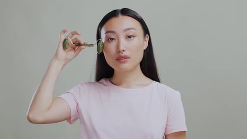 Young Attractive Korean Woman Massaging Face Gently with Green Stone Jade Roller Chinese Beauty Tool