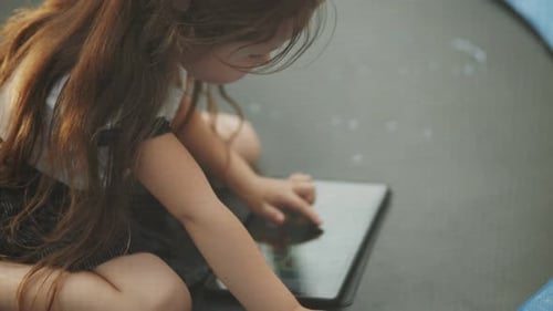 Child Sitting on a Trampoline and Looking at a Tablet