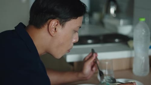 Asian Man Enjoying a Nutritious Green Salad While Sitting at a Small Kitchen Table