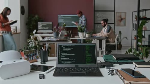 Laptop with Lines of Computer Code on Desk at Busy IT Startup during Workday