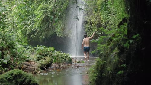 Man walking in front of waterfall in rainforest. Peaceful and Tranquil concept.
