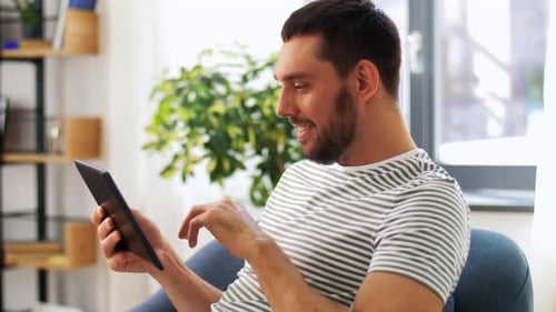 Man Smiles and Uses Tablet in Bright Home