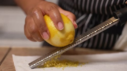 Black woman's hands seen zesting a lemon on a grater to use the peel shavings as a tasty ingredient