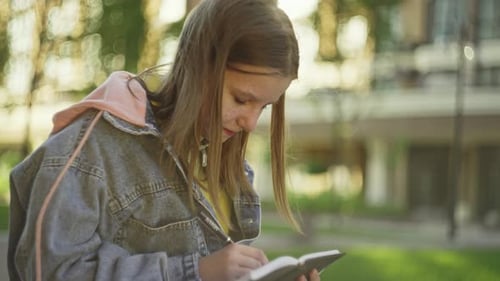 Teen Writing in Notebook Outdoors on Sunny Day