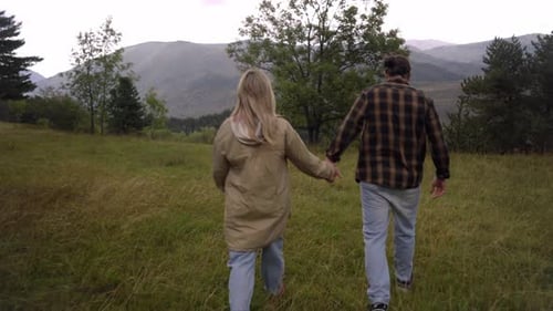 Rear View of Young Couple Holding Hands Walking Outdoor in the Nature