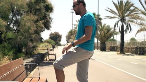 Young, Sporty Man Stretching Legs On Bench In City Park