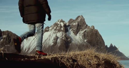 Man In Black Jacket Exploring Black Sand Beach With Snowy Mountains