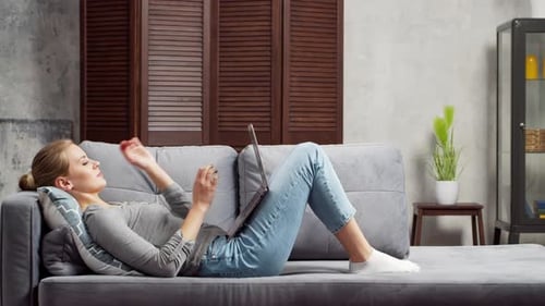 Young Woman Works Using a Laptop Lying on the Couch Student Entrepreneur or Freelancer Girl Working