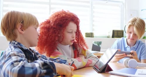 Caucasian Kids Sitting at Desk in Classroom and Using Tablet Device for Playing or Studying
