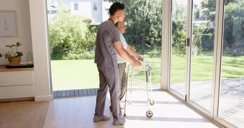 Physiotherapist assisting senior woman with walker in bright, sunlit room