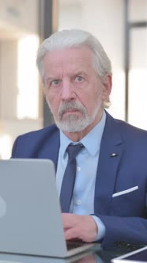 Old Businessman Looking at Camera while Working in Office, vertical video