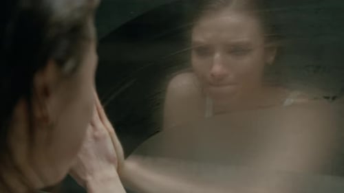 Chica emocionalmente desequilibrada limpiando un espejo brumoso y golpeándolo con el puño