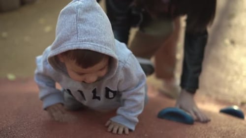 Mom Helps Her Son Climb the Slide A Boy on the Playground Climbs Up a Hill A Child in a Gray Hoodie