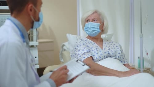Young Doctor Giving Consultation Visiting Senior Unhealthy Woman Recovering Illness in Hospital Room