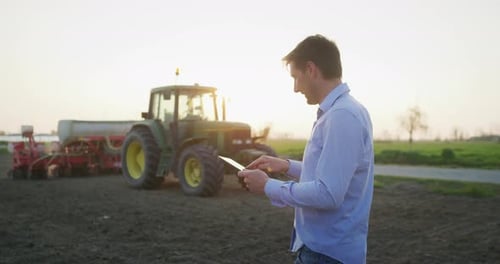 Farmer Using Tablet Beside Tractor at Sunset