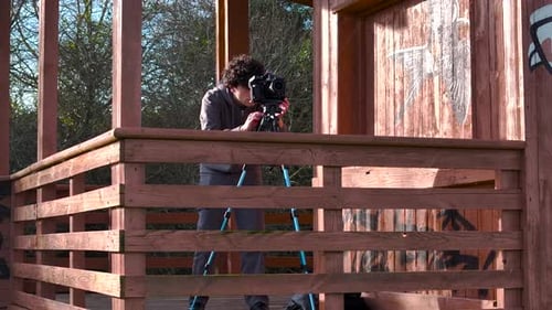 Outdoor Photographer Taking Pictures From Balcony Of Wooden Cabin In Forest. arc shot