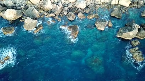 Drone shot panning upwards of a rocky, blue and clear ocean landscape in Malta.