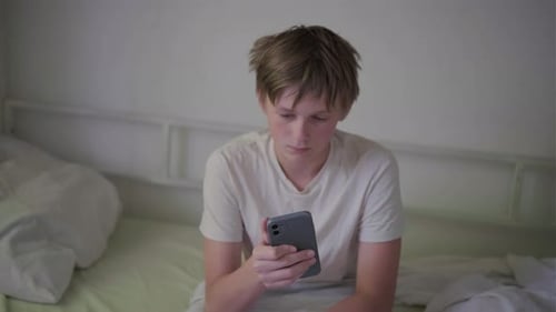 Teen Boy Using Smartphone Sitting on Bed