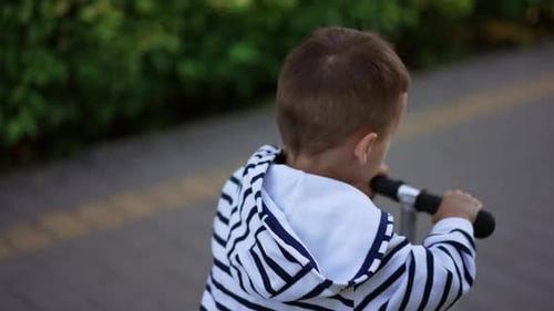 Lovely Caucasian kid riding a scooter in the park.