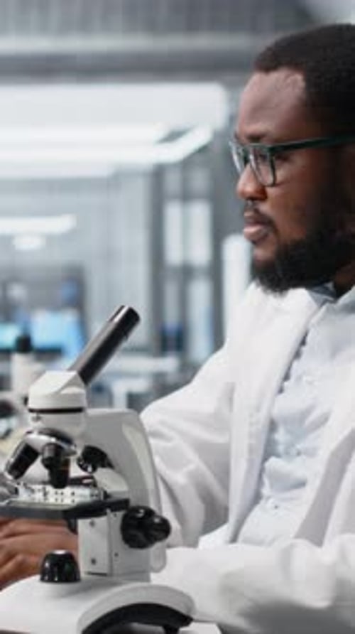 Man Adjusting Settings on Microscope in Bright Lab
