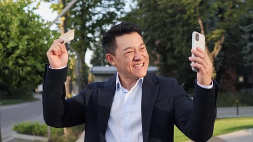Excited Man Holding Credit Card and Smartphone Outdoors