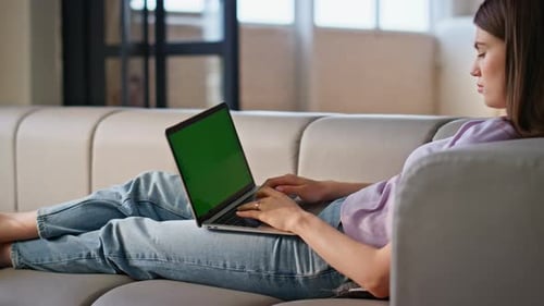 Woman Using Laptop with Green Screen on Couch