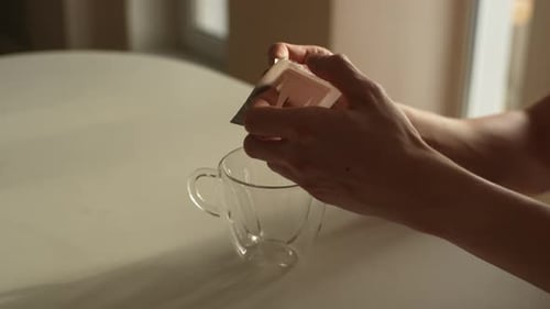 Closeup Highangle View of Unrecognizable Man Putting Bag of Drip Coffee in Glass Cup at Table in