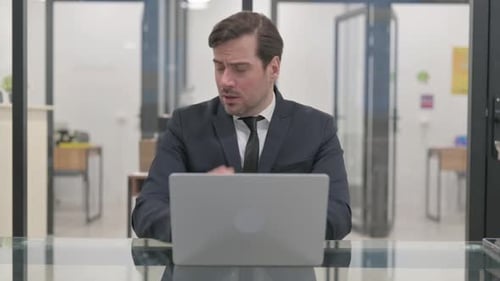 Man Coughing While Working at Laptop in Office