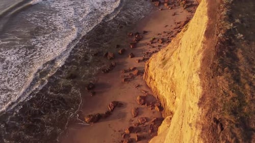 Top down aerial view of beach over cliff edge during sunset