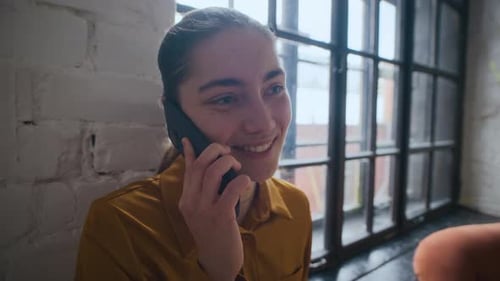 Smiling Woman Talking on Phone Indoors by Window