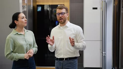 Seller Helping Young Woman Choosing Refrigerator in Appliance Store