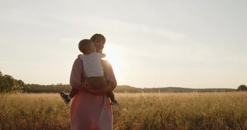 Happy Mother Spinning Her Son Holding Hands in a Golden Field at Sunset