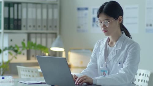 Asian Female General Practitioner Using Laptop at Work in Medical Office