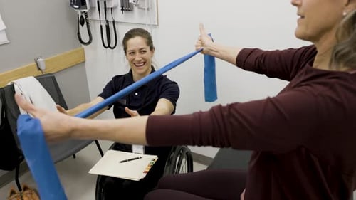 Physical therapist in wheelchair guides patient using resistance band at clinic
