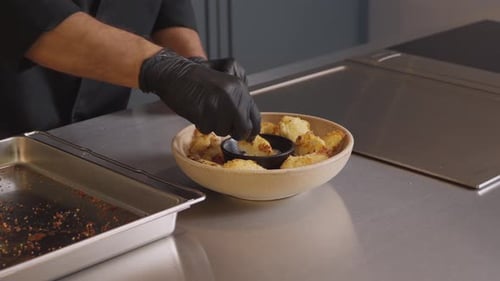Chef dips fried cauliflower in sauce at work