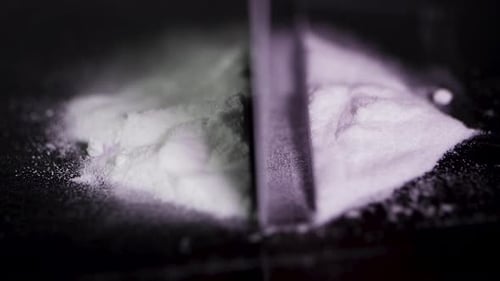Razor Blade Cutting Pile of White Powder on Dark Background