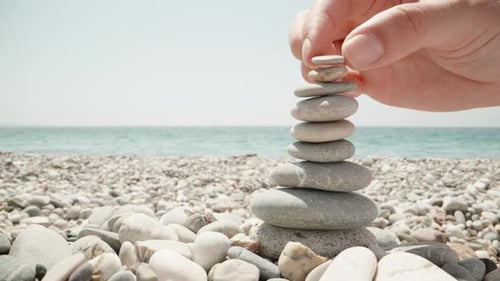 Close-up, a woman makes a cairn. Handmade stone tower on the seashore. A stack of balanced pebbles o
