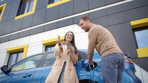 Couple of man and woman install charger plug from charging station to electric car before driving