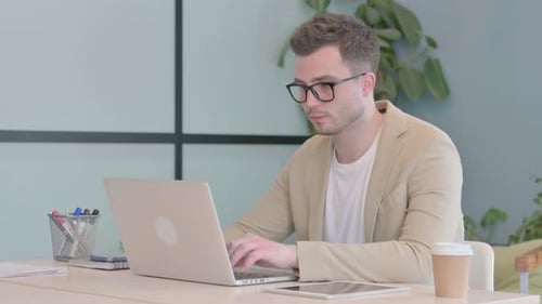 Young Man Typing on Laptop in Workplace