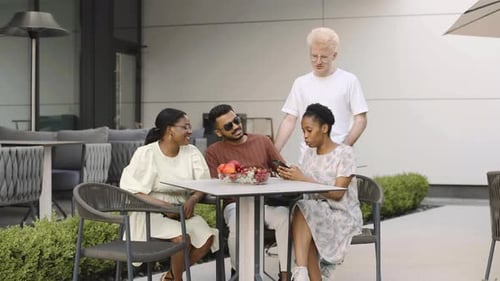 Friends relax and chat at an outdoor cafe. They enjoy cocktails and fresh fruit while taking