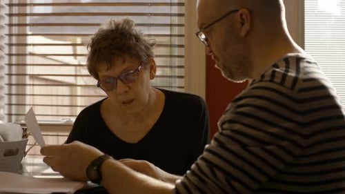 Senior Mother Sorting Documents With Help From Caregiver Son At Home On Spring Afternoon Medium Shot